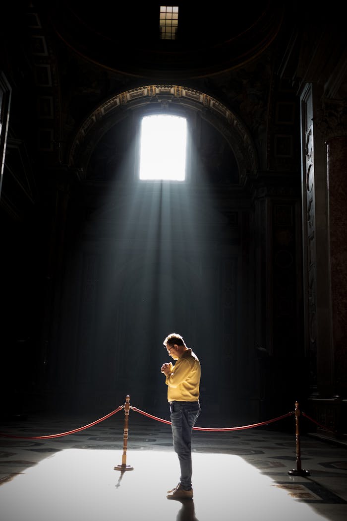 A man stands in prayer, illuminated by sunlight, in a tranquil Vatican City church.